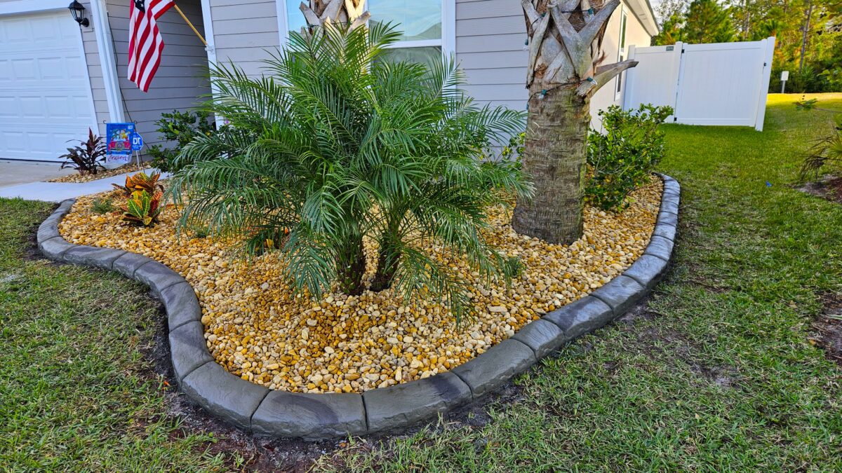 Decorative concrete curbing around a palm and river rock landscape bed in Palm Coast, FL