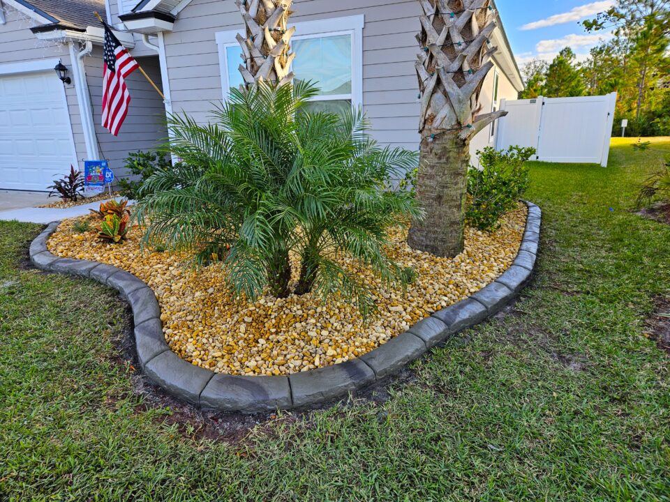 Decorative concrete curbing around a palm and river rock landscape bed in Palm Coast, FL