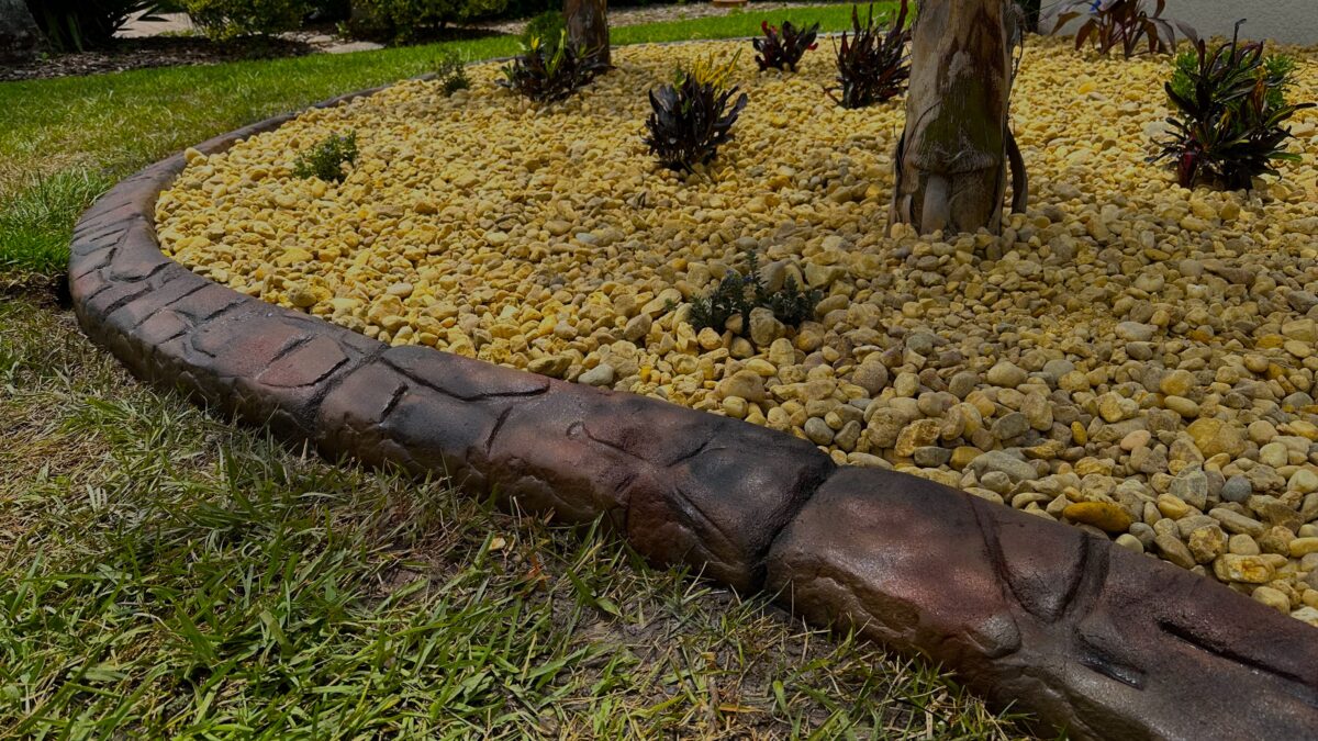 Curved stamped concrete curbing around a compact rock bed with bromeliads and palms at a Palm Coast, FL home