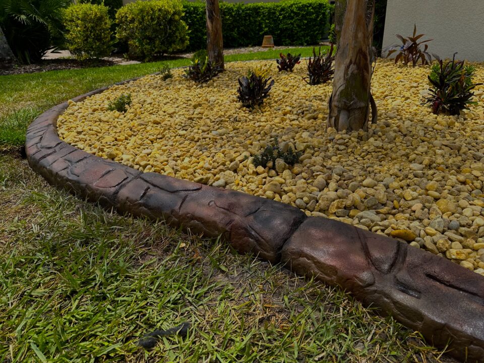 Curved stamped concrete curbing around a compact rock bed with bromeliads and palms at a Palm Coast, FL home